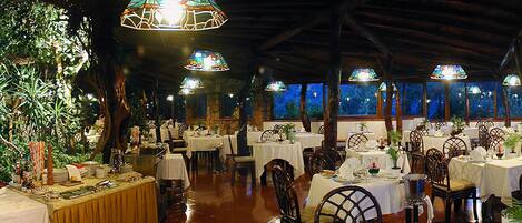 Un restaurante con varias mesas dispuestas para comer, rodeado de amplios vitrales y vigas de madera en el techo.