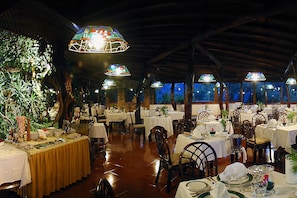 A restaurant with multiple tables set for dining, surrounded by large stained glass windows and wooden beams on the ceiling.