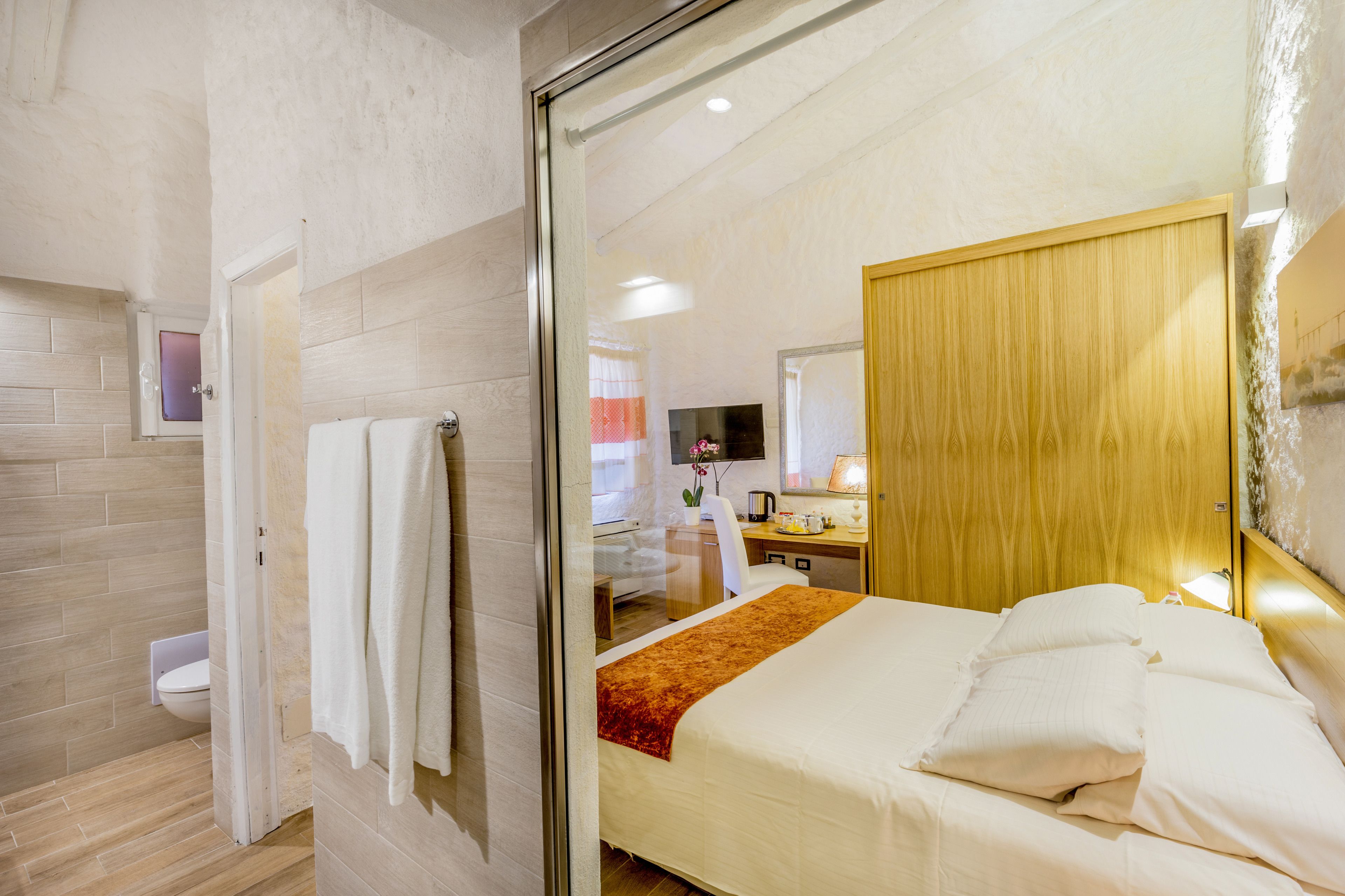 A hotel room with a bed, a desk, a chair, a mirror, and a bathroom visible through an open door.