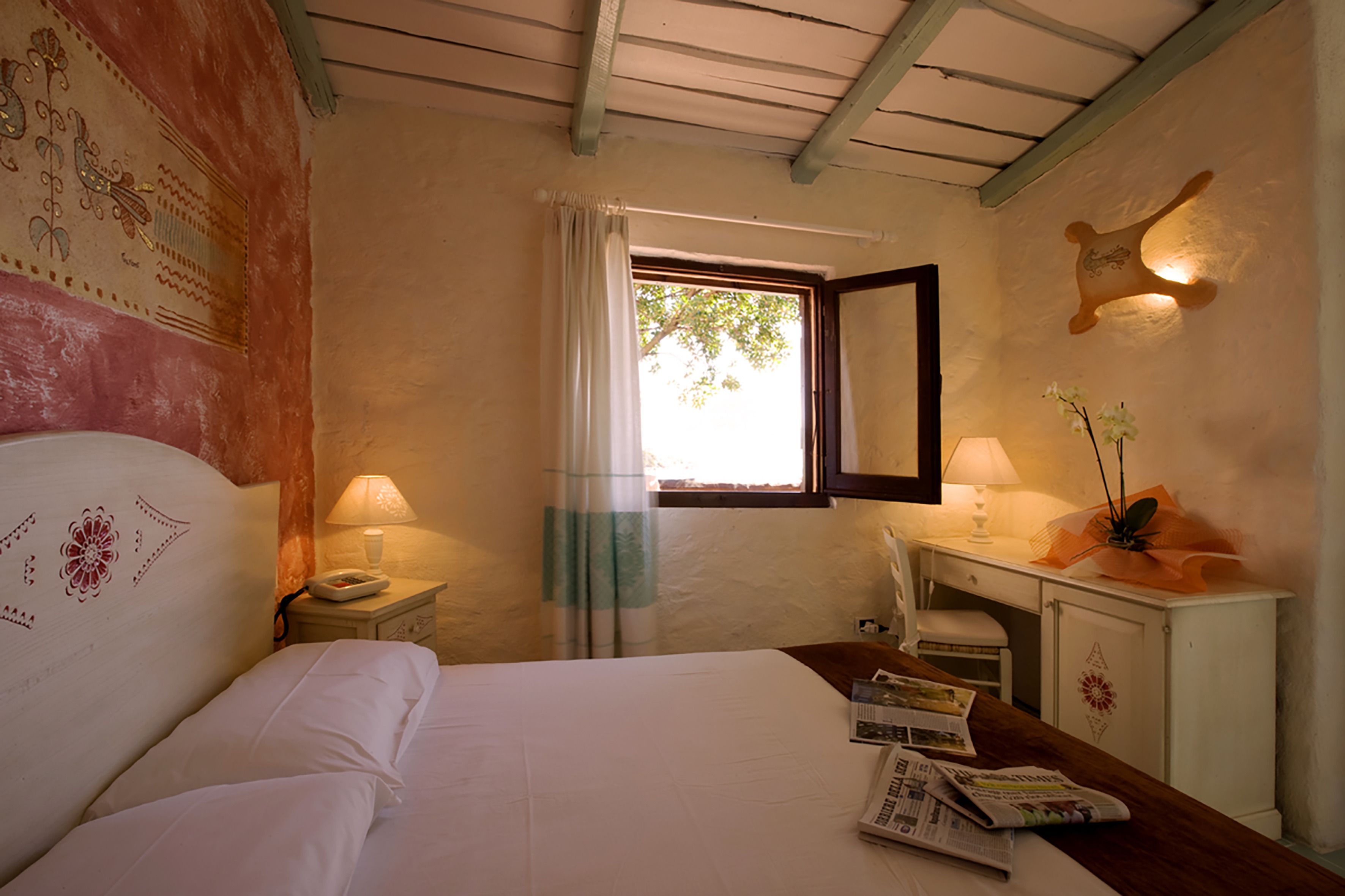 Un dormitorio con cama, mesita de noche, lámpara y ventana con cortinas.