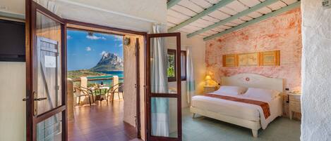 Un dormitorio con cama, mesita de noche y vista a un paisaje montañoso a través de una puerta abierta.