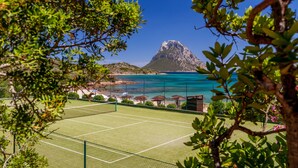 A tennis court with a view of a mountain and the sea.