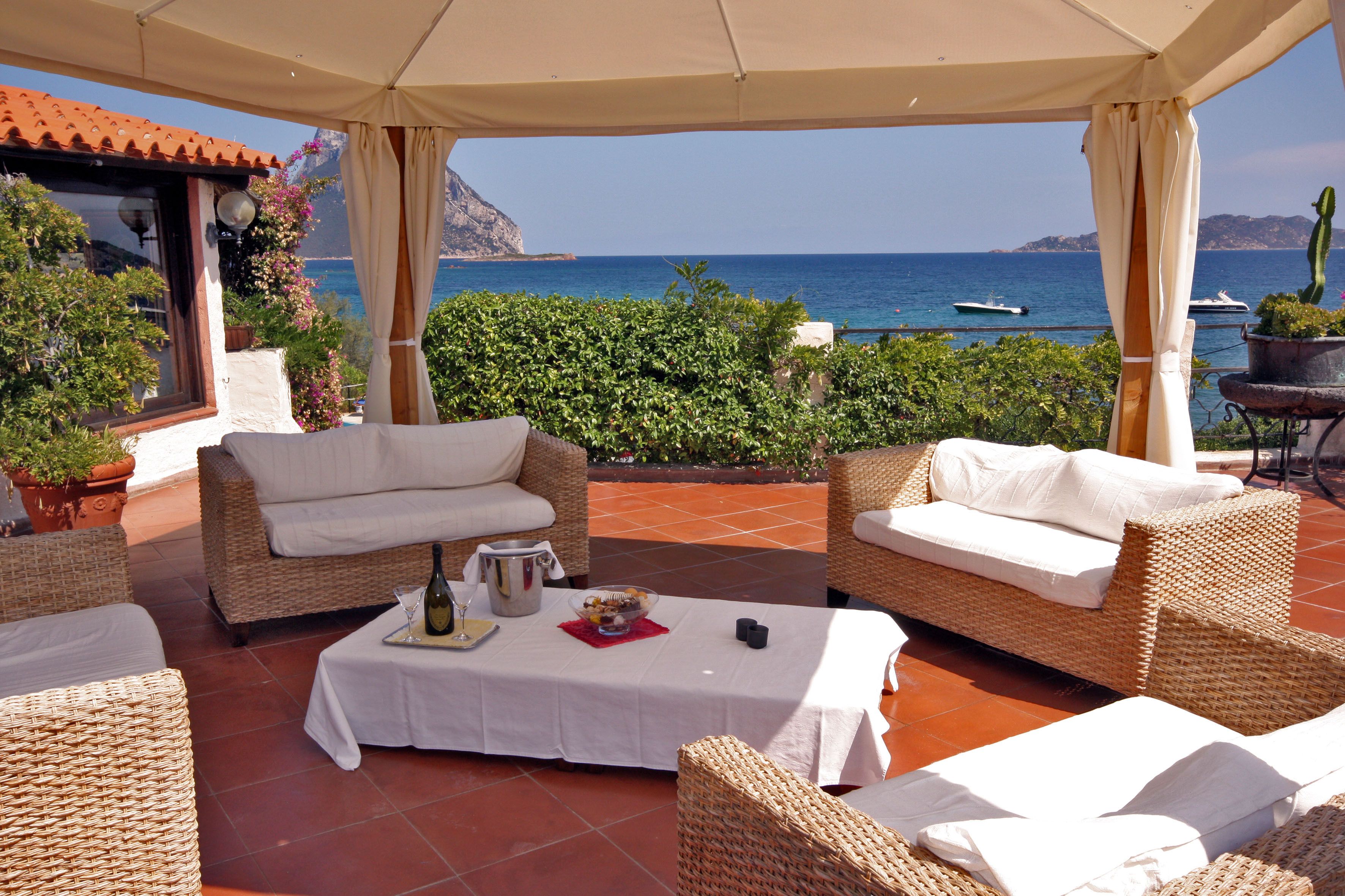 Un espacio de estar al aire libre cubierto con mobiliario de mimbre, una mesa con mantel blanco y vistas al mar.