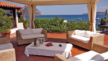 Un espacio de estar al aire libre cubierto con mobiliario de mimbre, una mesa con mantel blanco y vistas al mar.