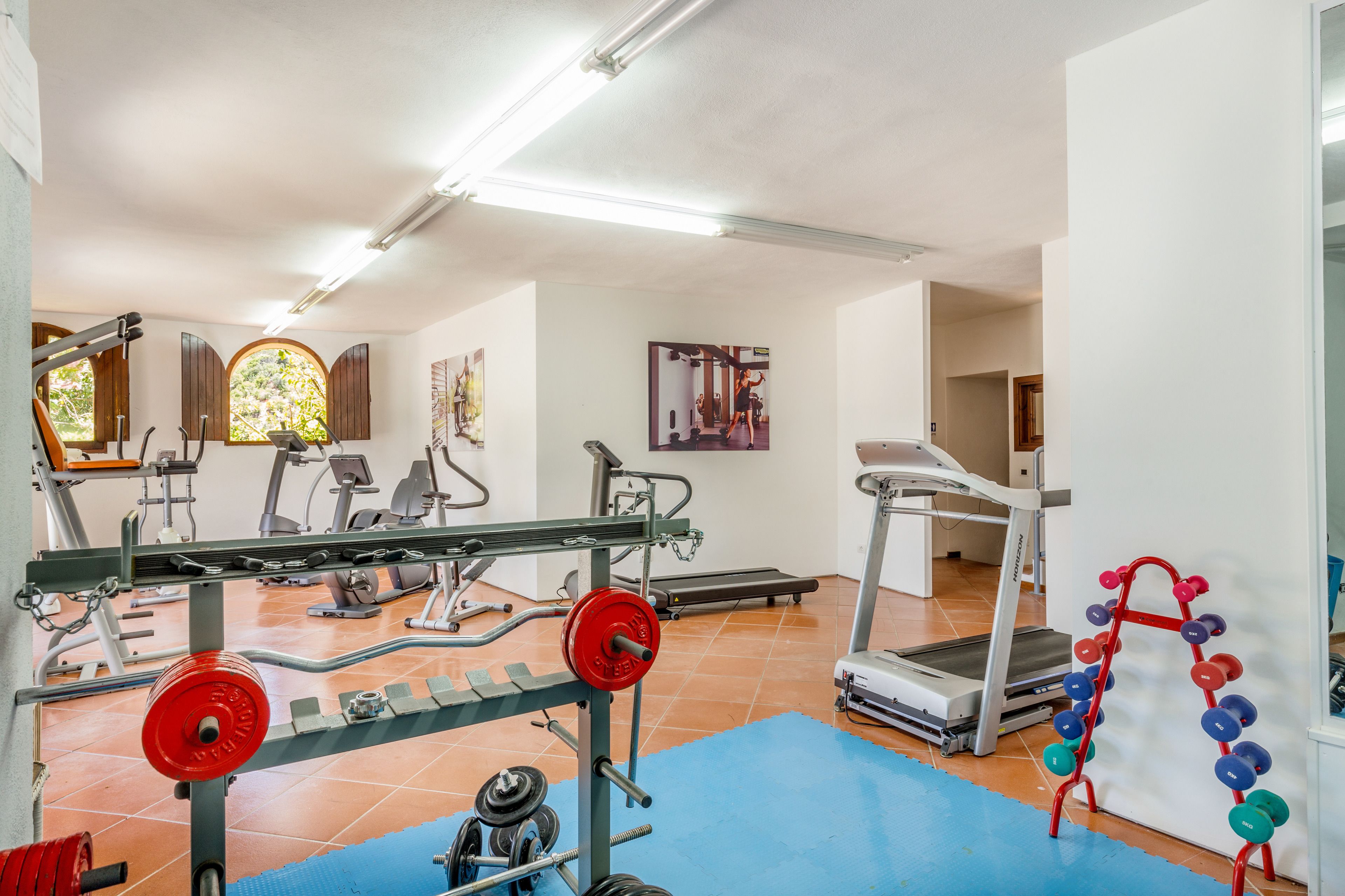 Ein Fitnessraum mit Trainingsgeräten, einem Laufband und einer blauen Yogamatte.