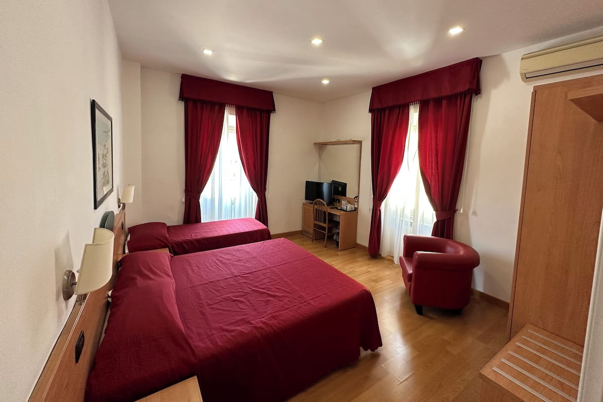 A hotel room with two beds, a desk with a computer, a chair, and a wardrobe.