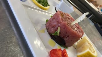 Une assiette avec une brochette de viande crue, garnie de citron et de tomates.