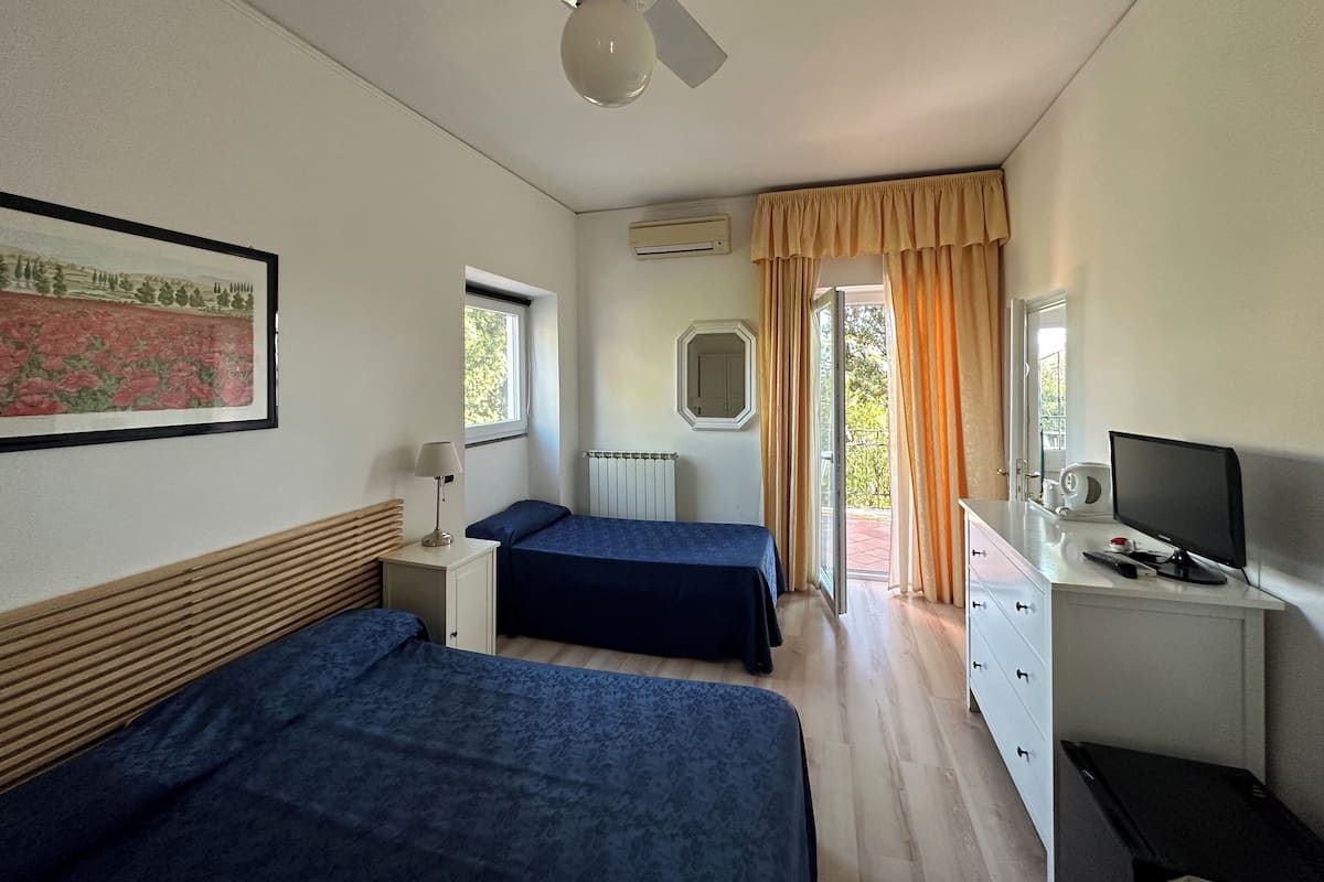 A bedroom with two beds, a ceiling fan, a window with curtains, a radiator, and a desk with a computer.