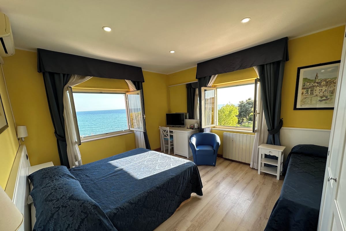 A hotel room with a bed, a desk, a chair, and a view of the sea.