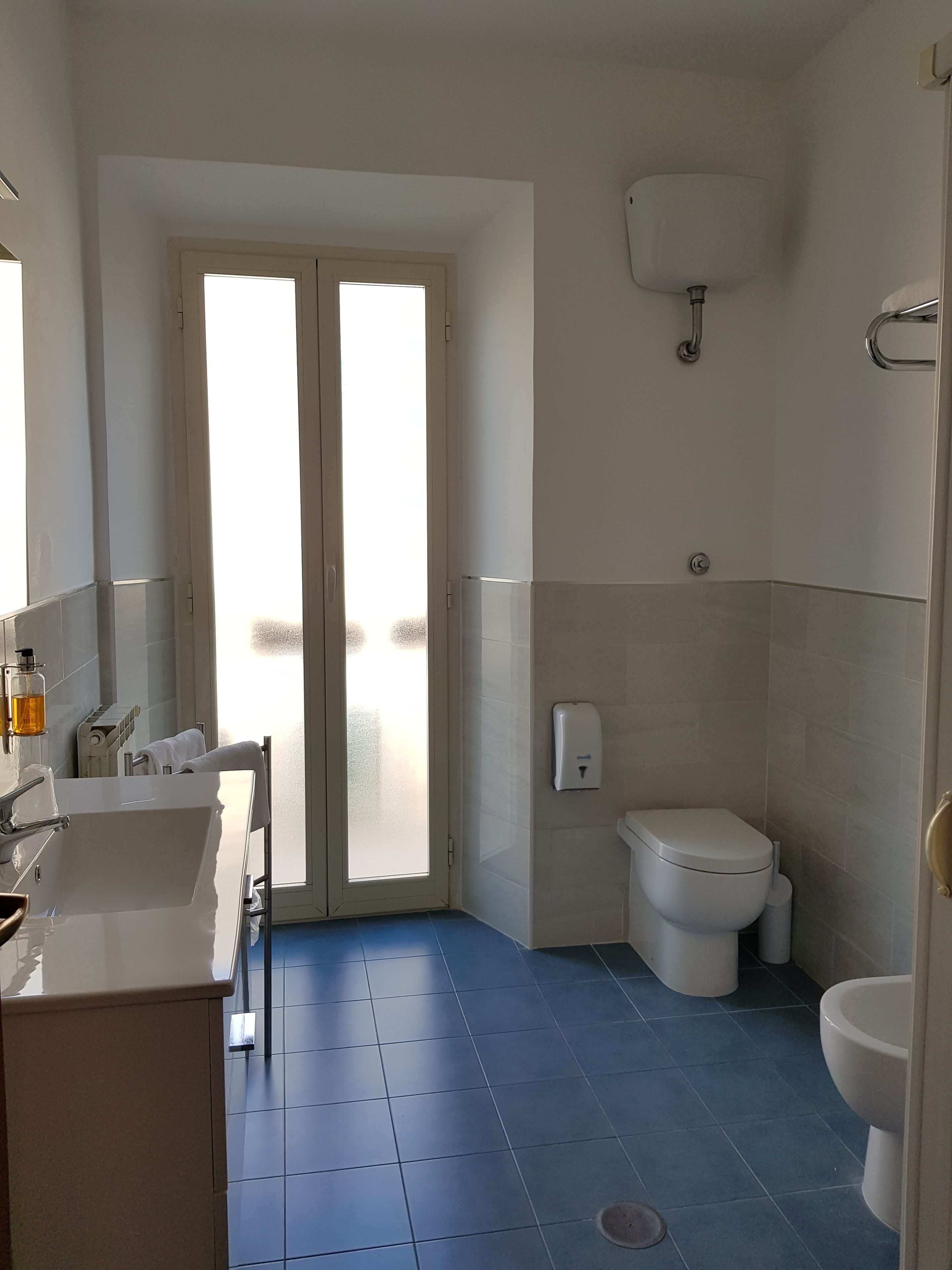 Un baño con lavamanos blanco, inodoro y bidé, suelo de baldosas y puerta de vidrio esmerilado.