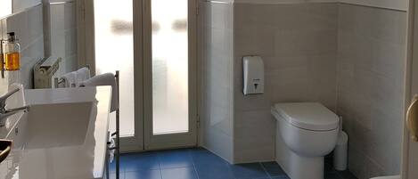 Un baño con lavamanos blanco, inodoro y bidé, suelo de baldosas y puerta de vidrio esmerilado.
