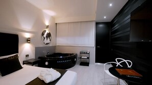 A modern hotel room with a large bed, a black bathtub, a small table with a book, and a TV mounted on the wall. - Hotel Motel Visconteo (Binasco)