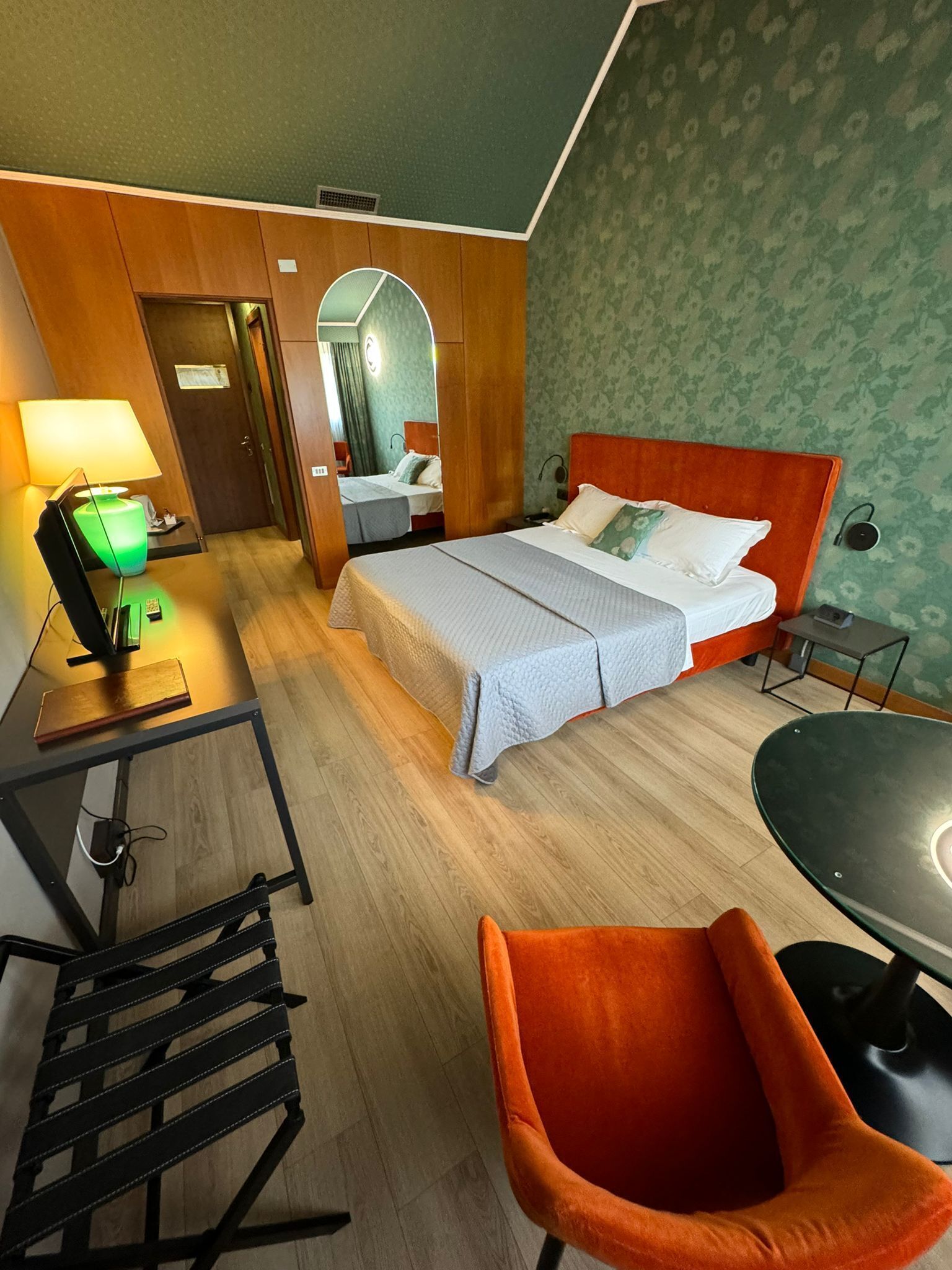 A hotel room with a bed, a desk with a lamp, a chair, and a table.