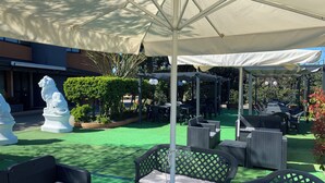 An outdoor patio area with green artificial turf, wicker furniture, and white umbrellas providing shade. - Hotel Motel Visconteo (Binasco)