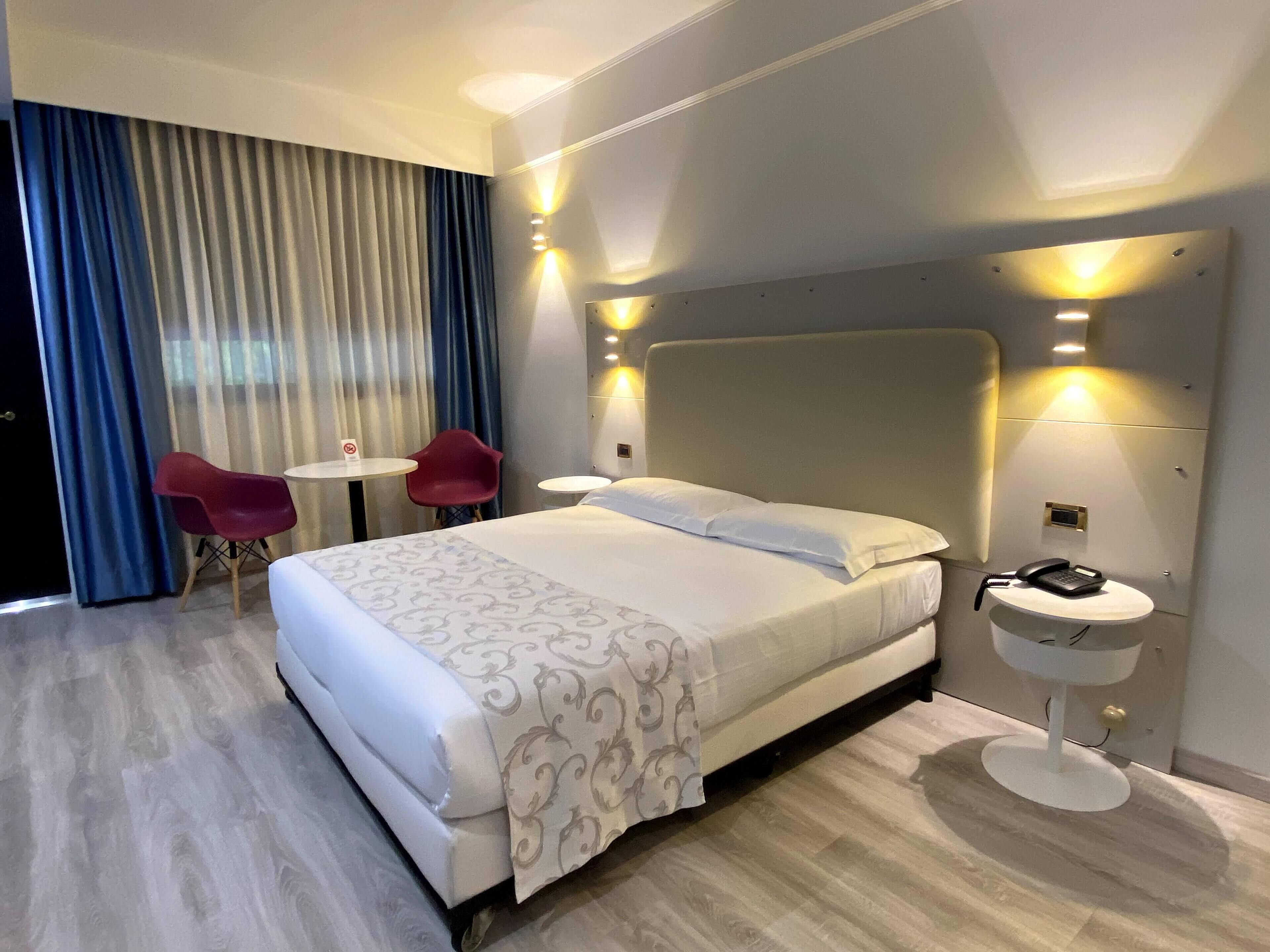 A hotel room with a large bed, a small desk, a chair, and a phone on the bedside table.