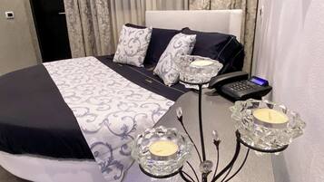 Un dormitorio moderno con una cama bien hecha, una mesita de noche con un teléfono y un candelabro, y una lámpara fijada a la pared.