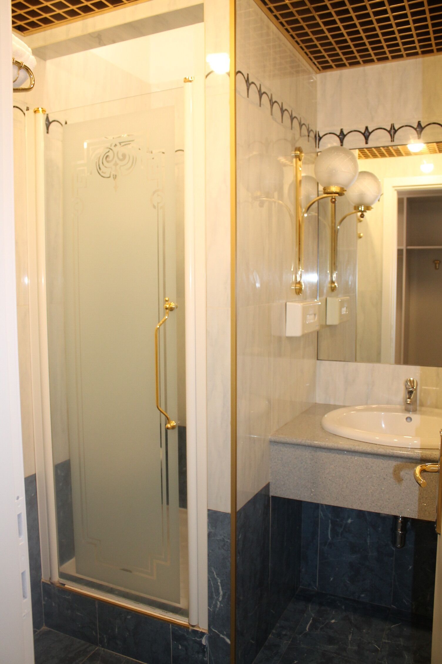 A glass-enclosed shower with a gold handle, a white sink with a gold faucet, and a mirror above the sink.