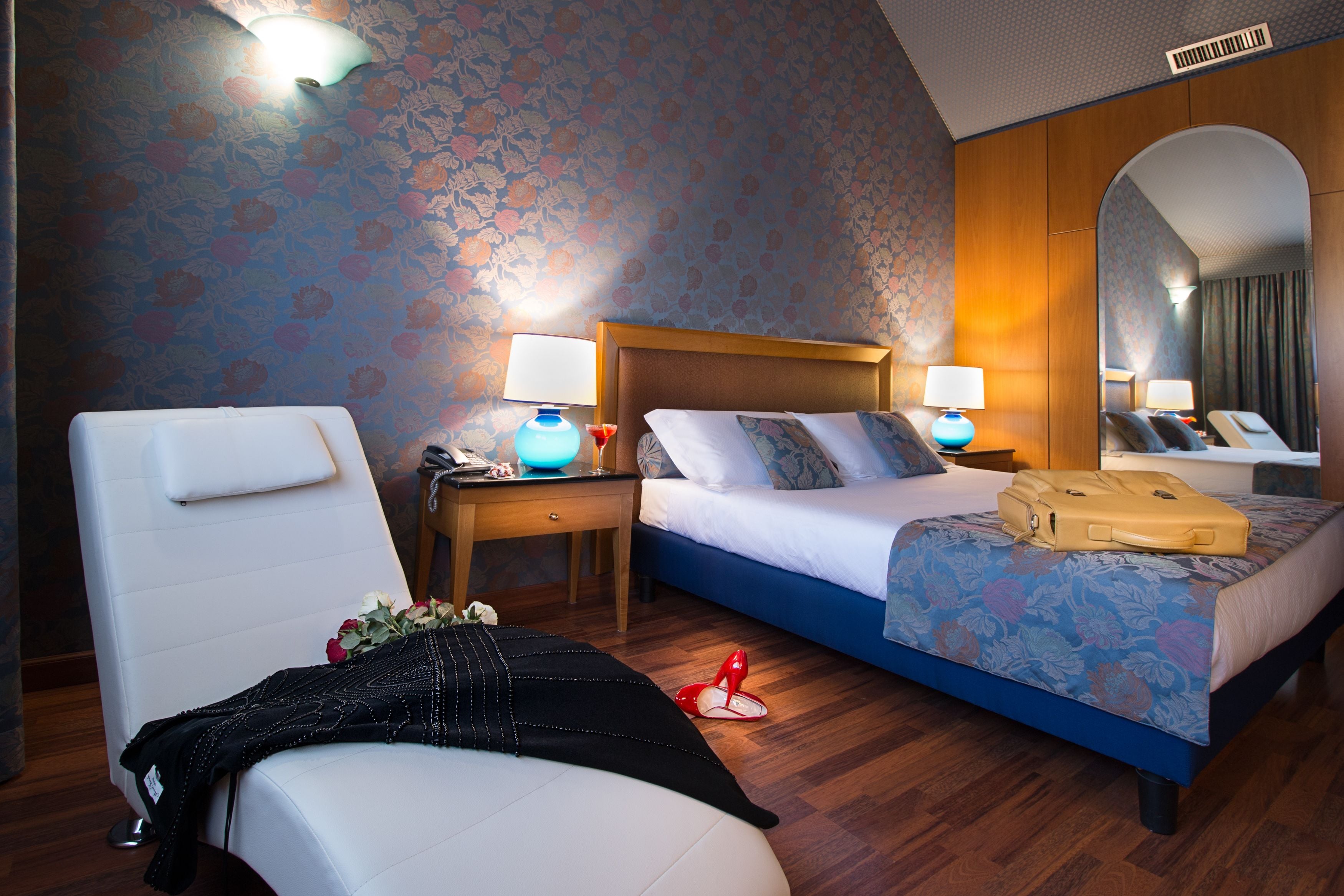 Ein Hotelzimmer mit Bett, Stuhl, Nachttisch mit Lampe, Spiegel und Koffer auf dem Bett.