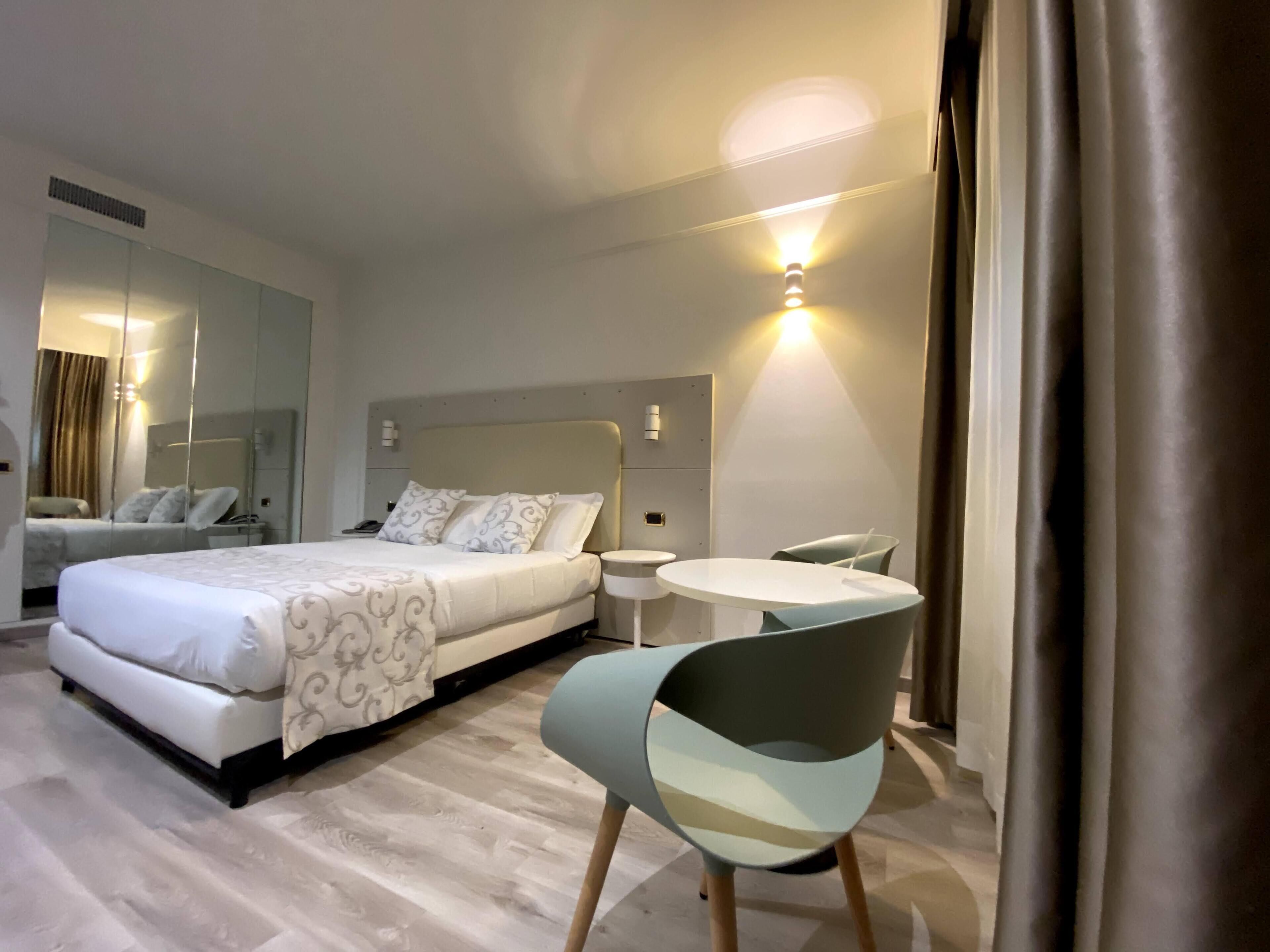 Et moderne hotelværelse med en stor seng, et natbord, en stol og et lille rundt bord.