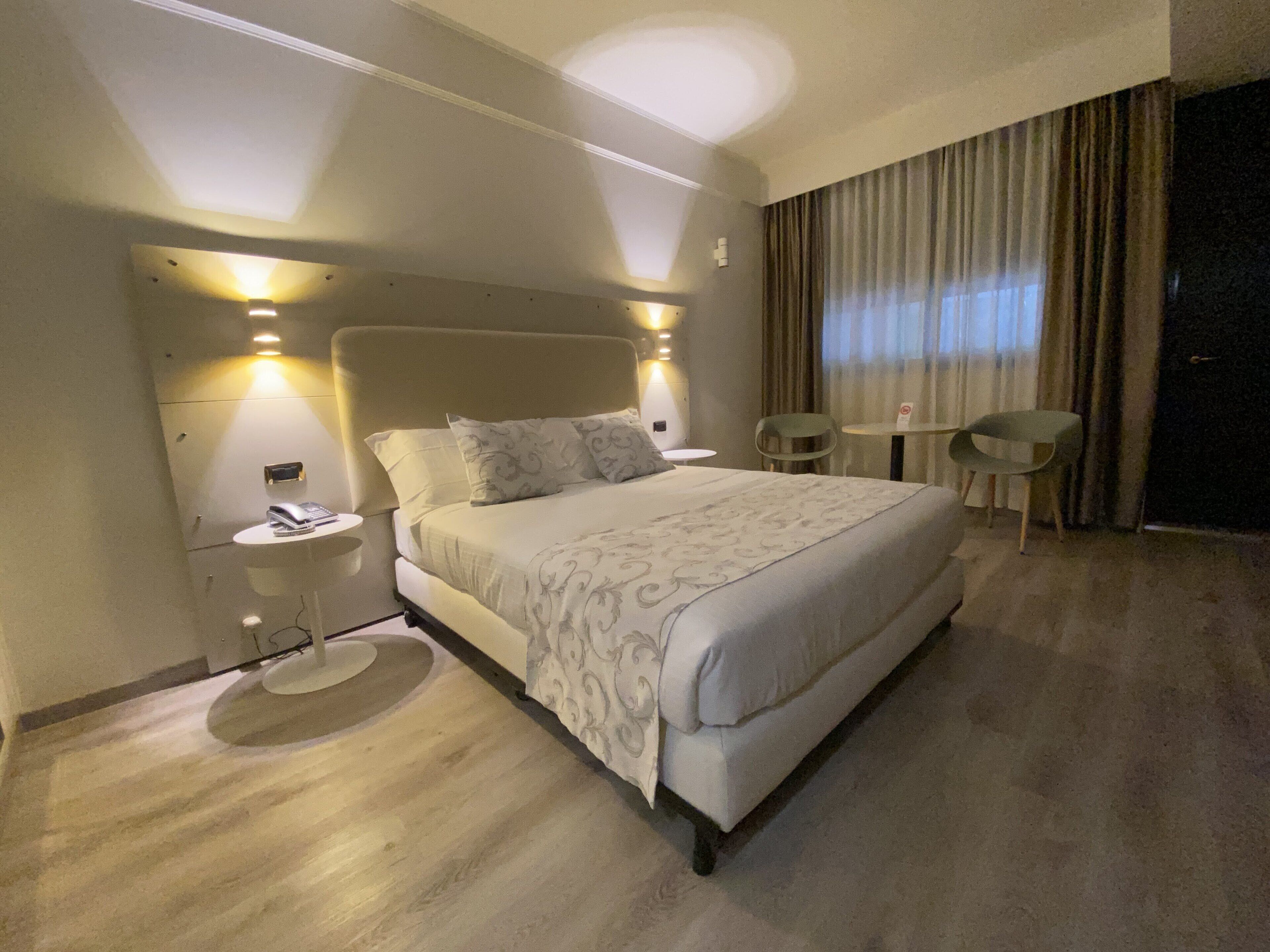 Una habitación de hotel moderna con una cama grande, mesitas de noche, una pequeña mesa redonda y una silla.
