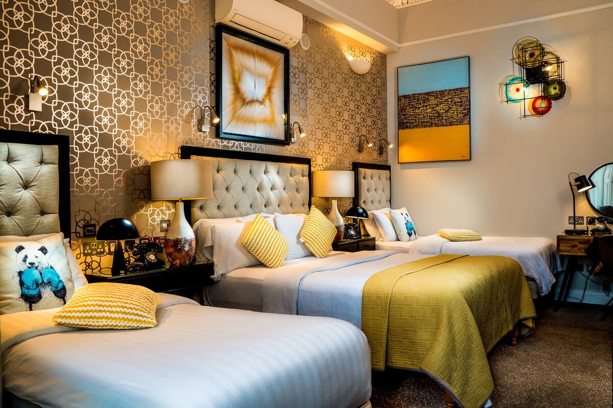 Quarto de hotel com duas camas, uma janela grande e uma escrivaninha com cadeira.