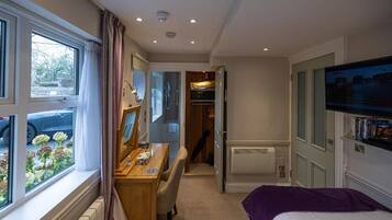 A bedroom with a bed, a desk, and a window overlooking a garden.