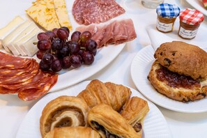 A variety of food items including cheese, cured meats, grapes, and pastries on a table.