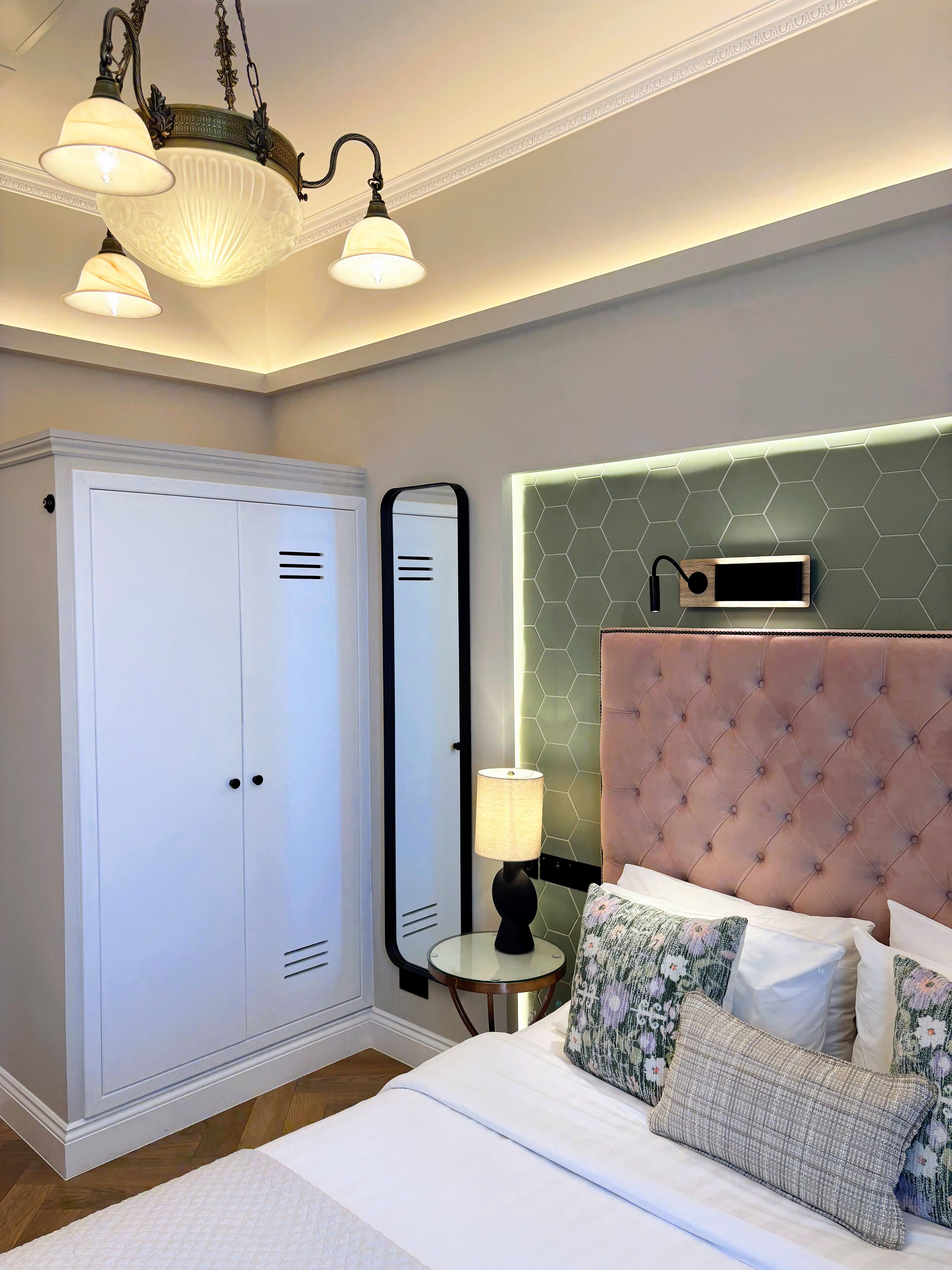 Un dormitorio con cama, mesita de noche con lámpara, armario, espejo y cabecera con altavoz.