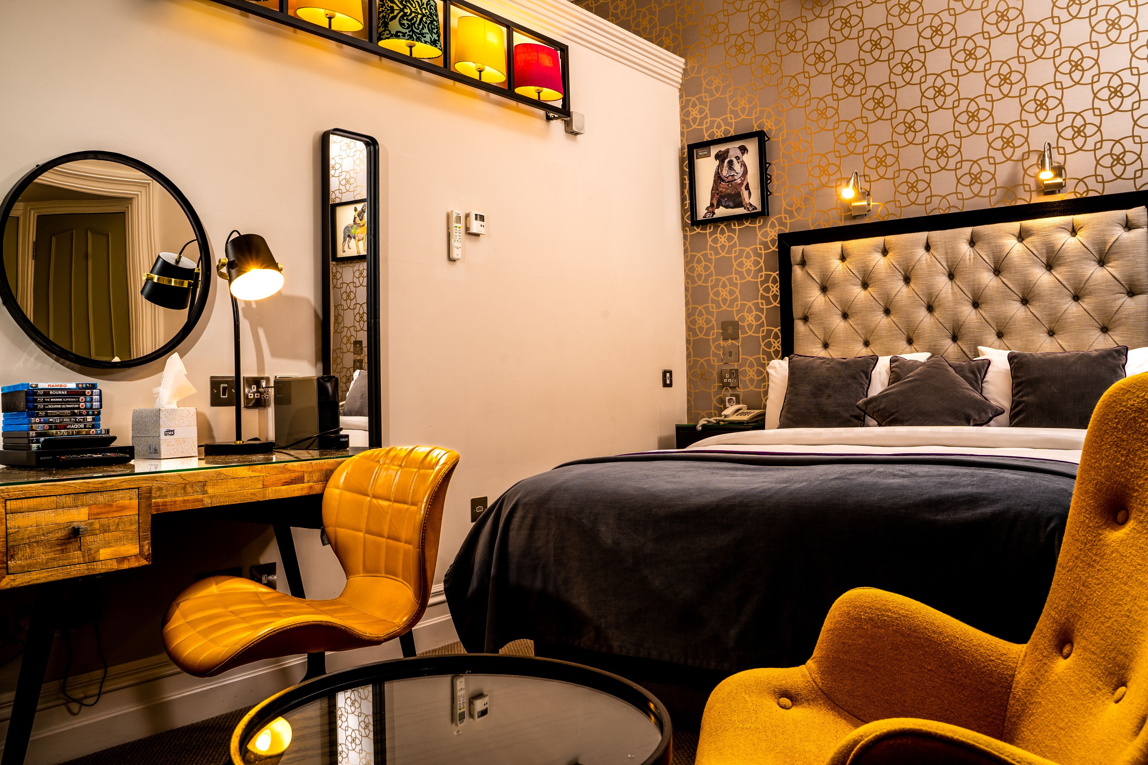 Una camera d'albergo con un letto, una scrivania, una sedia, uno specchio e una parete con carta da parati decorata.