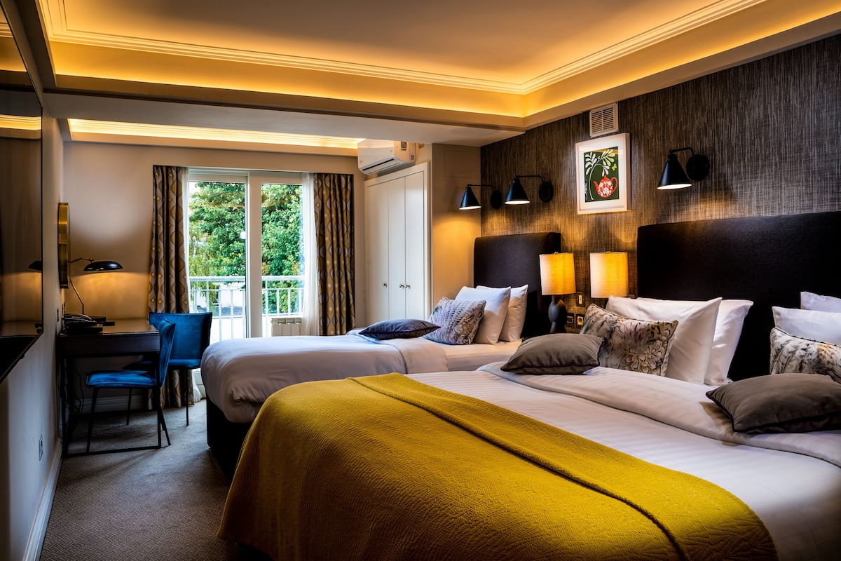 Quarto de hotel com duas camas, uma escrivaninha com cadeira, uma janela com cortinas e uma varanda.