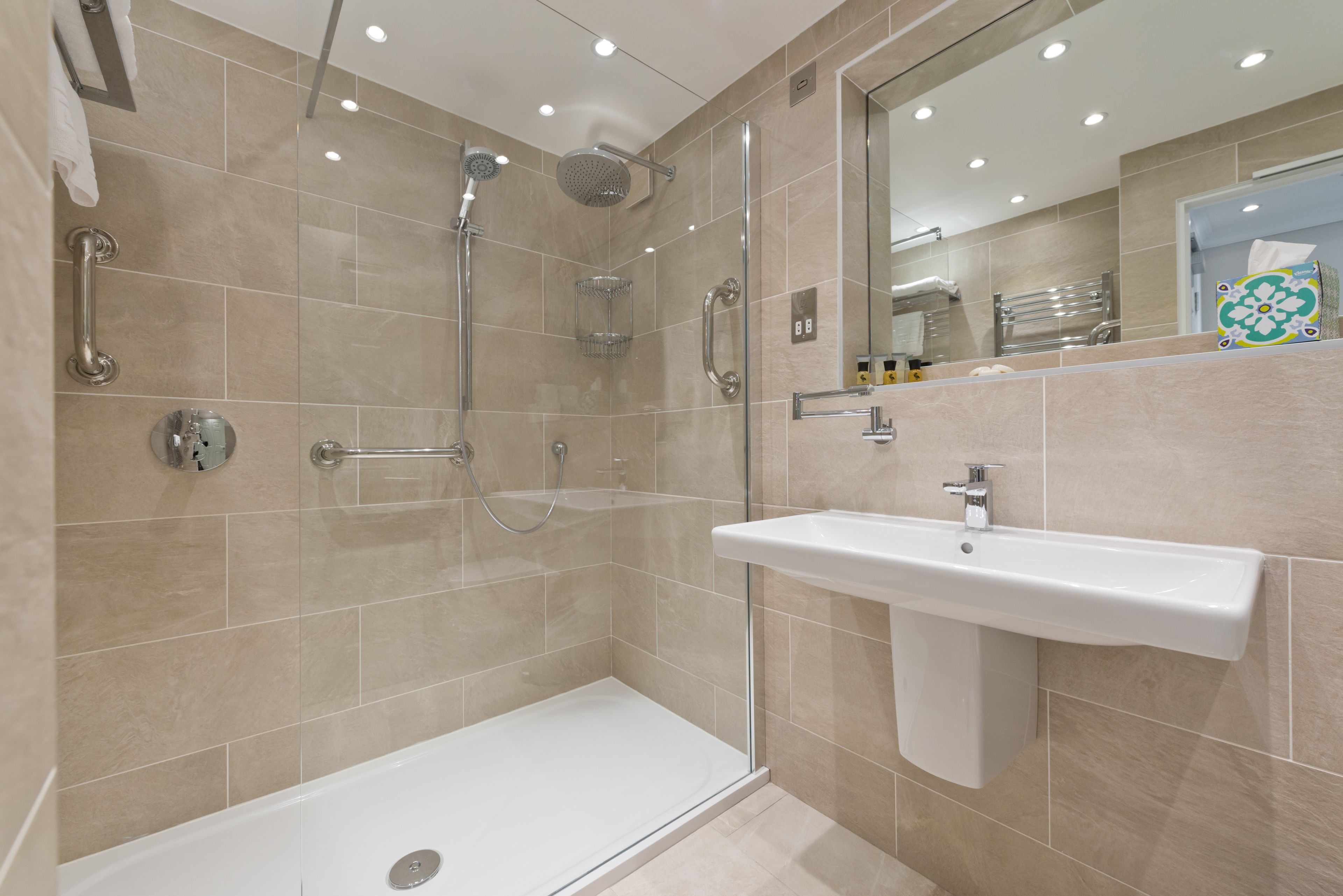 Un baño moderno con ducha a ras de suelo, zona de ducha con mampara de cristal, un lavabo blanco y un espejo sobre el lavabo.