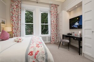 Un dormitorio con cama, escritorio, silla, televisión y ventana con cortinas.