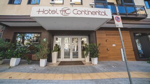 The entrance to Hotel Continental with a clear glass facade, potted plants, and a no parking sign.