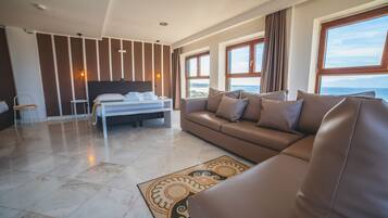 A modern hotel room with a large bed, a sofa, and a view of the sea.