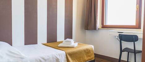 Een hotelkamer met een bed, een stoel, een bureau en een raam met gordijnen.