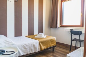 Una habitación de hotel con una cama, una silla, un escritorio y una ventana con cortinas.