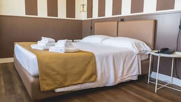 Un letto rifatto con una coperta marrone e lenzuola bianche, un comodino con un telefono, e una parete a righe verticali marroni e bianche.