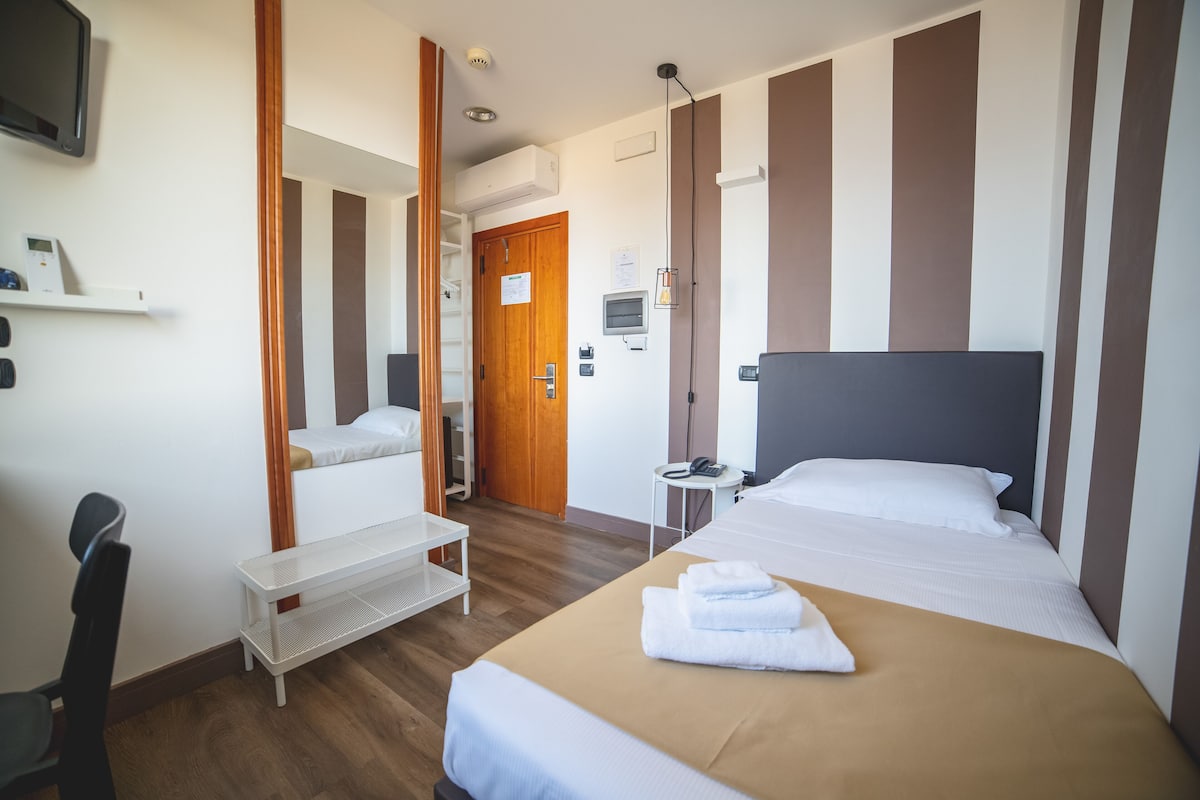 Een hotelkamer met een bed, een bureau, een stoel, een nachtkastje, een spiegel en een deur.