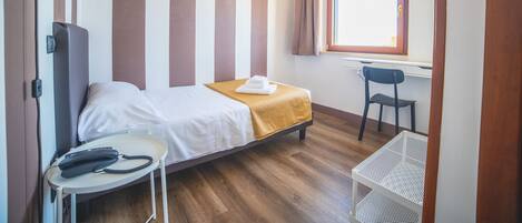 Une chambre d’hôtel comprenant un lit, un bureau avec un téléphone, une chaise, une fenêtre avec des rideaux et un luminaire suspendu.