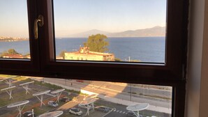 A view from a window overlooking a coastal area with a road and parked cars below.