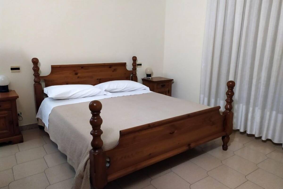 A wooden bed with a headboard, two bedside tables, and a white curtain.