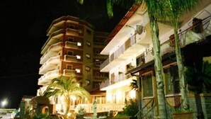 A multi-story hotel with balconies, palm trees, and a well-lit facade. - Casa del Gourmet (Siderno)