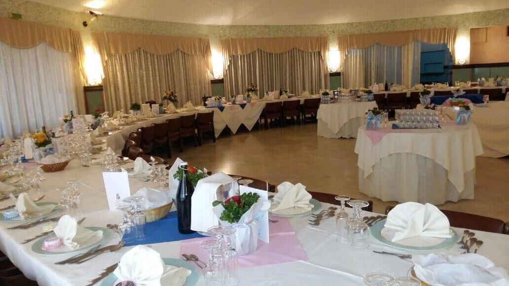 A banquet hall with round tables set for a formal event, featuring white tablecloths, glassware, and floral centerpieces.