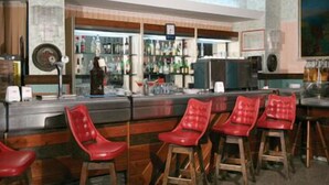 A bar area with wooden stools and a counter with various bottles and glasses. - Casa del Gourmet (Siderno)