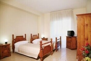 Un dormitorio con una cama de madera, una mesita de noche, un televisor sobre un mueble de madera y una ventana con cortinas.