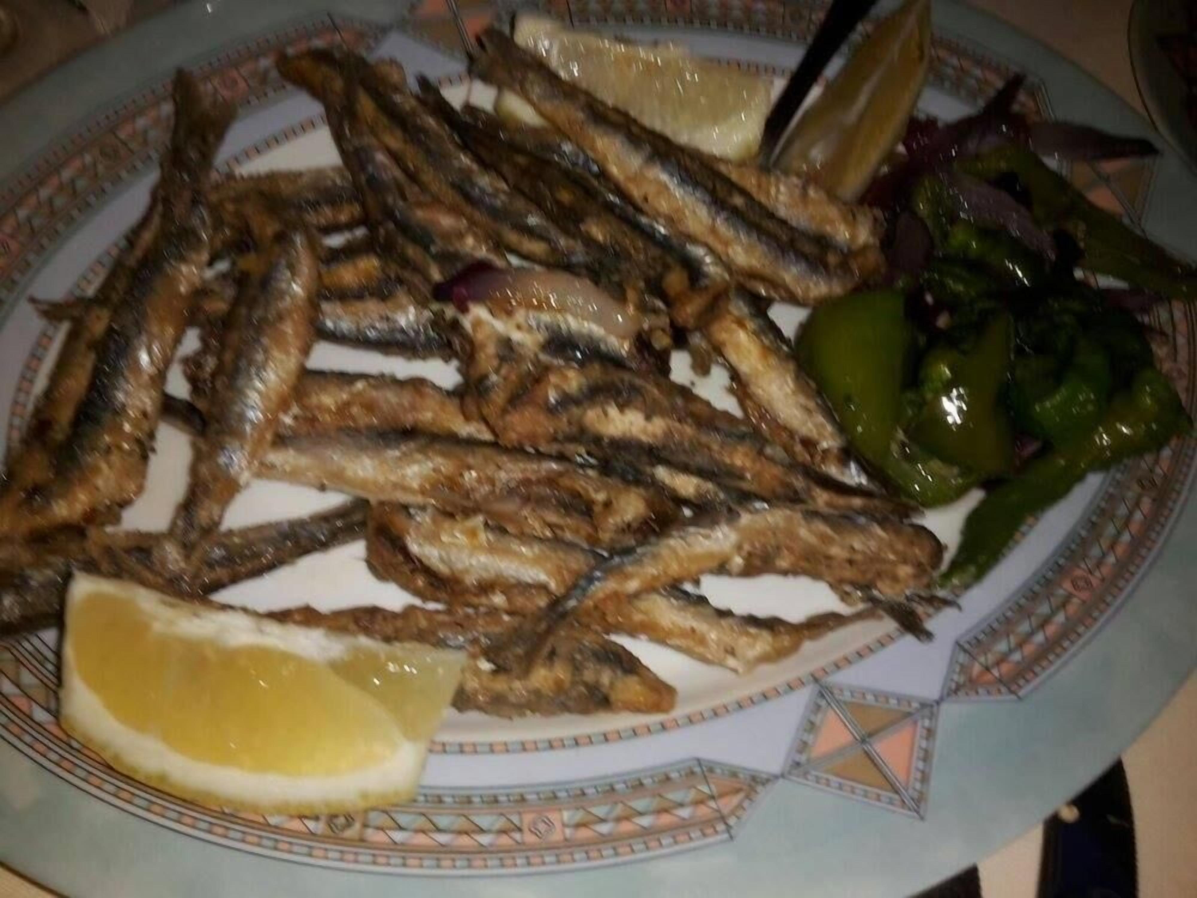 Un plato de pescado a la parrilla con cuñas de limón y una ensalada.