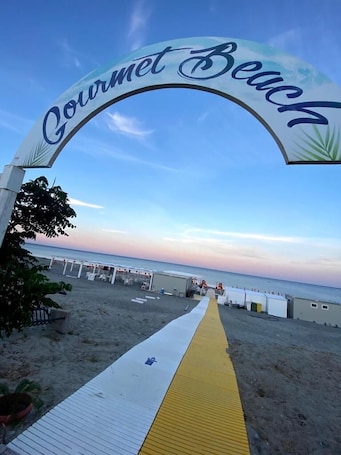 A beach entrance archway with the text "Gourmet Beach" and a pathway leading to beachside accommodations.