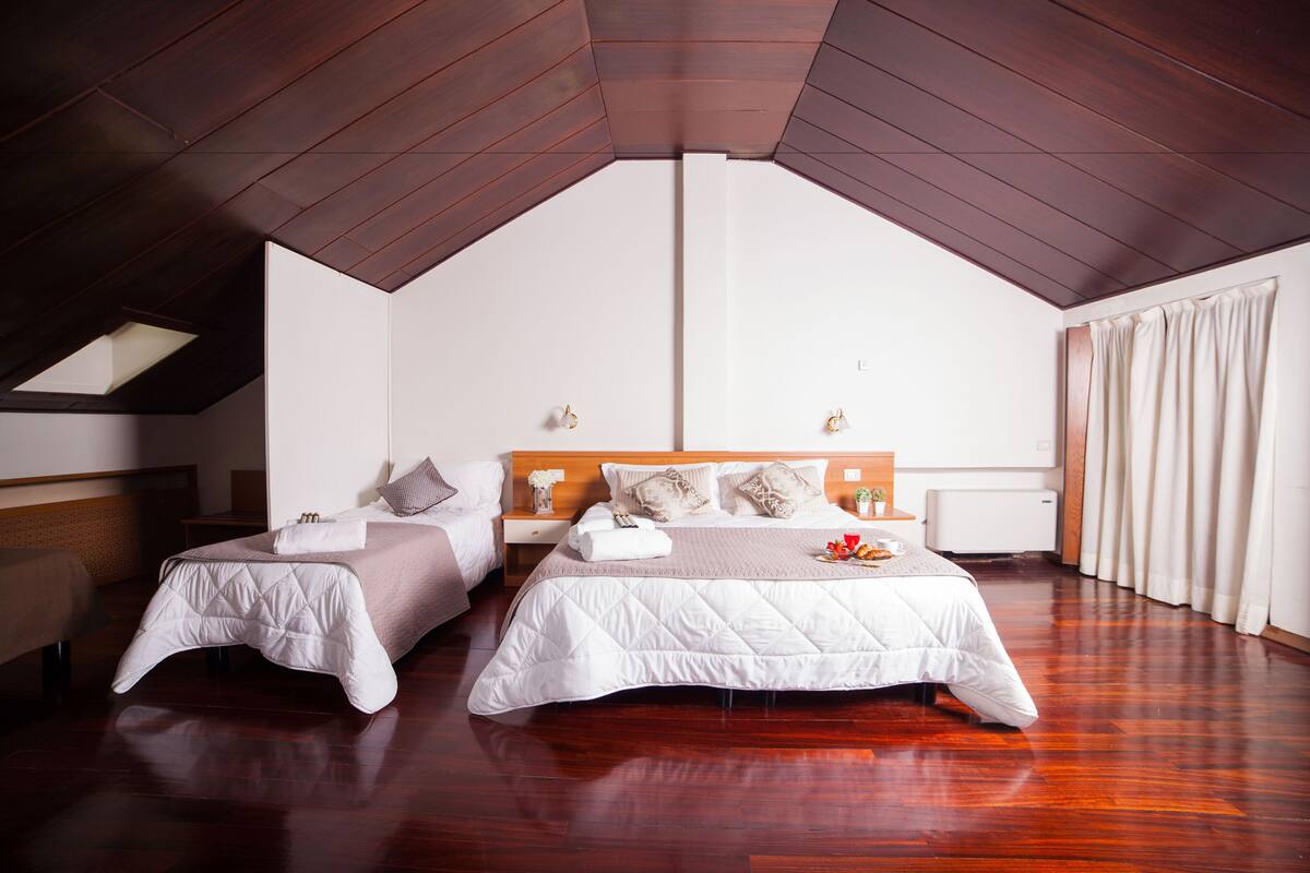 A bedroom with two beds, wooden flooring, a sloped ceiling, and a large window.
