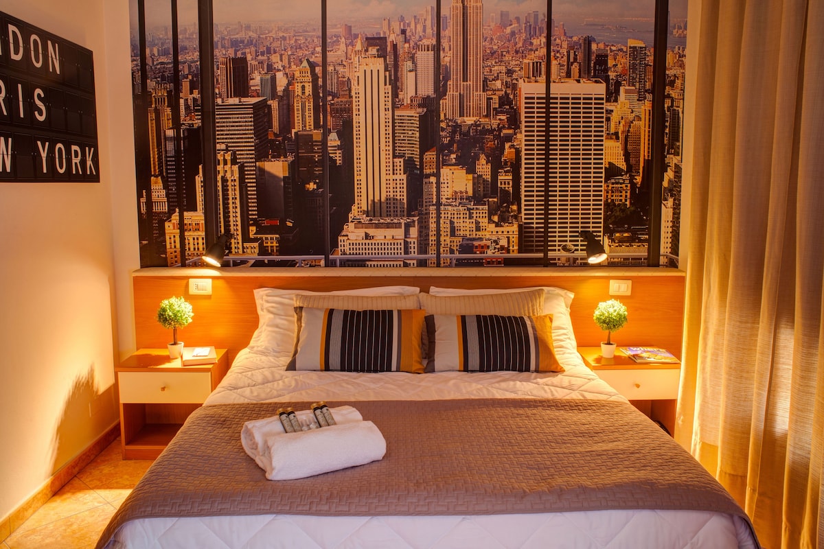 Une chambre d’hôtel offrant une vue imprenable sur la ville, un lit parfaitement fait, deux tables de chevet avec des lampes et un panneau accroché au mur.