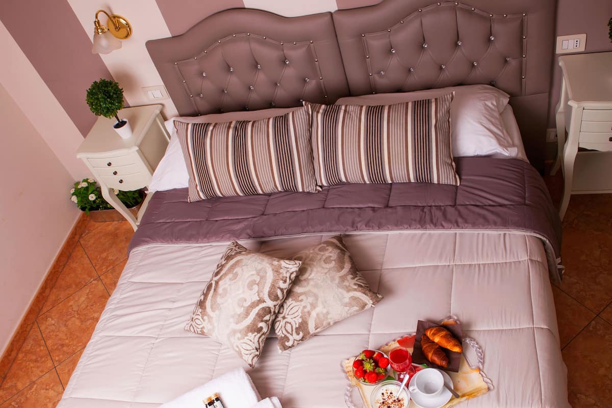 A neatly made bed with a striped pillow set, a decorative headboard, and a tray with breakfast items.